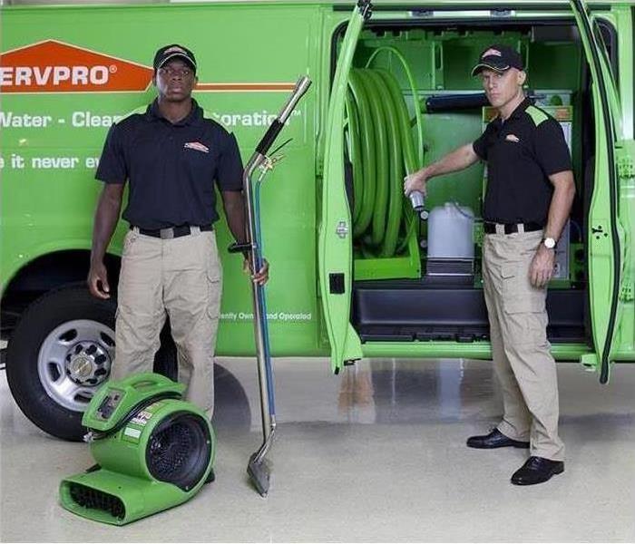 Two men standing by a SERVPRO van holding drying equipment.